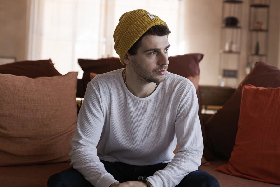 young man in yellow cap and white shirt sitting on sofa looking sideways